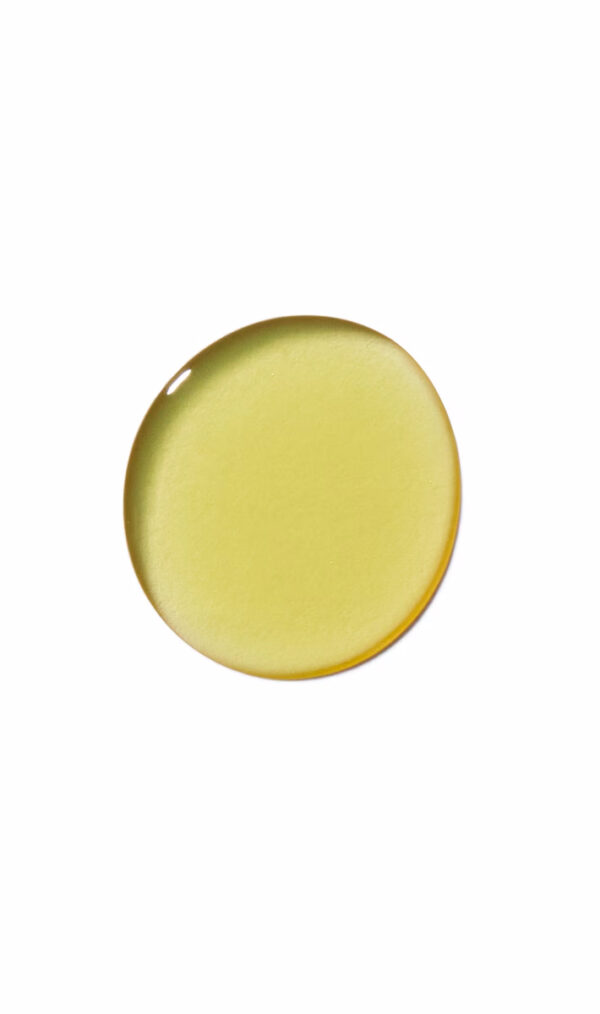 A close-up of a single droplet of Invati advanced scalp revitalizer, showing its yellow-colored liquid on a white background. - SAAB Salon Spa | Ottawa On, Canada