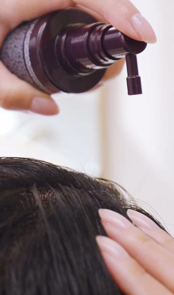 A person applies Invati Advanced Scalp Revitalizer to their scalp using a dark-colored pump dispenser, while another hand touches the hair near the application area. - SAAB Salon Spa | Ottawa On, Canada