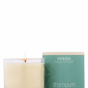 A lit Shampure Candle in a clear glass container next to its cylindrical green cardboard packaging. - SAAB Salon Spa | Ottawa On, Canada