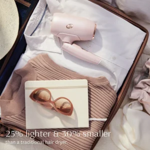 Open suitcase with neatly packed clothes, a folded white shirt, beige sweater, pink sunglasses, a white notebook, and the compact T3 Fit pink hair dryer. - SAAB Salon Spa | Ottawa On, Canada