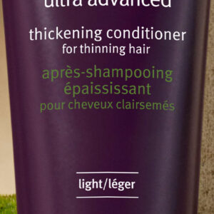 A bottle of Invati Ultra Advanced Thickening Conditioner - Light for thinning hair placed against a green background. Text on the bottle mentions it nourishes and thickens thinning hair immediately. - SAAB Salon Spa | Ottawa On, Canada