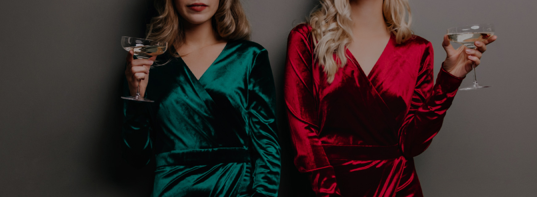 Two women in velvet dresses, one green and one red, holding champagne glasses against a gray background. - SAAB Salon Spa | Ottawa On, Canada