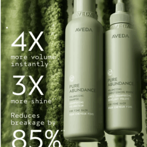 Two bottles of Pure Abundance Volumizing Shampoo by Aveda stand upright against a green textured background, with text emphasizing volume, shine, and reduced breakage benefits. - SAAB Salon Spa | Ottawa On, Canada