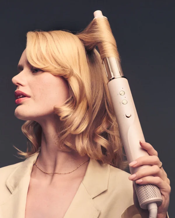 A blonde woman curls her hair with the T3 Aire360, a large cylindrical automatic curling iron, against a dark background. - SAAB Salon Spa | Ottawa On, Canada