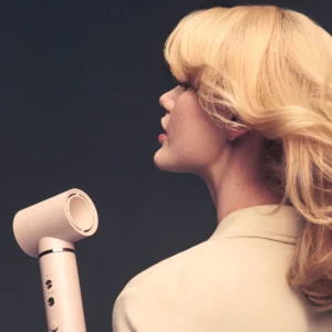 A person with blonde, wavy hair holds the T3 Aire360 hair dryer, facing sideways against a dark background. - SAAB Salon Spa | Ottawa On, Canada