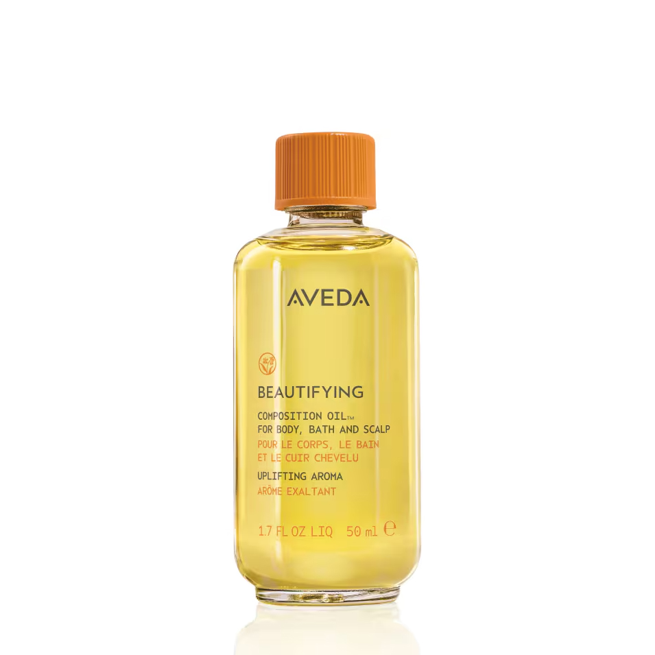 Clear glass bottle of Beautifying Composition Oil with a light yellow body and an orange screw cap. - SAAB Salon Spa | Ottawa On, Canada